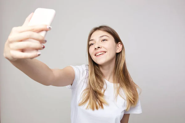 Chica feliz vestida con una camiseta blanca hace selfie sobre un fondo blanco en el estudio — Foto de Stock