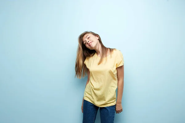 Lachende meisje gekleed in een geel t-shirt en jeans is op een blauwe achtergrond in de studio — Stockfoto