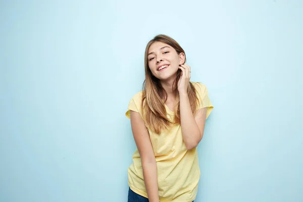 Lachende meisje gekleed in een geel t-shirt en jeans is op een blauwe achtergrond in de studio — Stockfoto