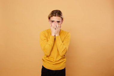 Sarı kazak giymiş sarışın adam ellerini stüdyoda bej arka yüzünde tutar