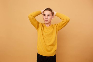 Sarı kazak giymiş genç sarışın adam ellerini kafasına stüdyo bej arka planda tutar