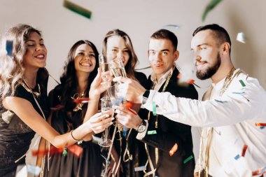 Güzel genç kızlar ve erkekler şık şık giysileriyle gülümseme birlikte ve kodes bardak şampanya studio lezzetli beyaz bir arka plan ile giyinmiş. Parti zamanı