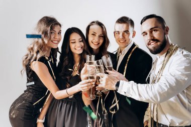 Güzel genç kızlar ve erkekler şık şık giysileriyle gülümseme birlikte ve kodes bardak şampanya studio lezzetli beyaz bir arka plan ile giyinmiş. Parti zamanı