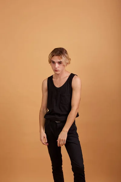 Молодий блондин, одягнений в чорну футболку і штани позує в студії на бежевому фоні — стокове фото