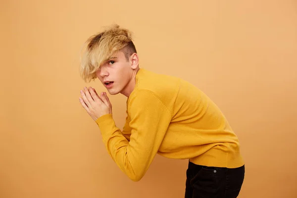 Стильний блондин, одягнений в жовтий светр і чорні джинси, позує на бежевому фоні в студії — стокове фото