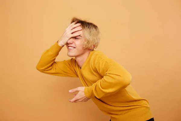 Stylový Blondýna chlap oblečený v žlutém svetru je pózovat s rukou na hlavě na béžové pozadí v ateliéru — Stock fotografie