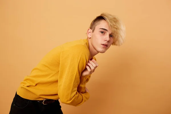 Стильний блондин, одягнений в жовтий светр і чорні джинси, позує на бежевому фоні в студії — стокове фото