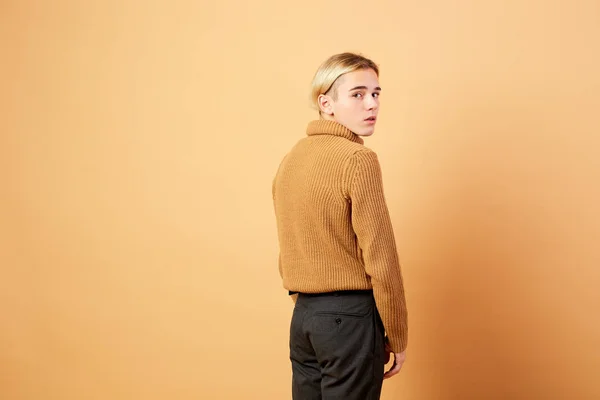 Mladá blondýna chlap oblečený v hořčičné barvy svetr a černé kalhoty pózuje v ateliéru na béžové pozadí — Stock fotografie