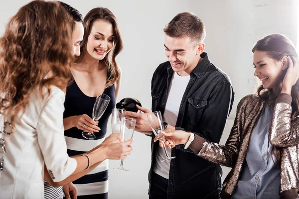 Kızlar ve şık rahat kıyafetler giymiş çocuklar yan yana ve gülümse. Adam şampanya gözlükte yağıyor. Parti ruh hali