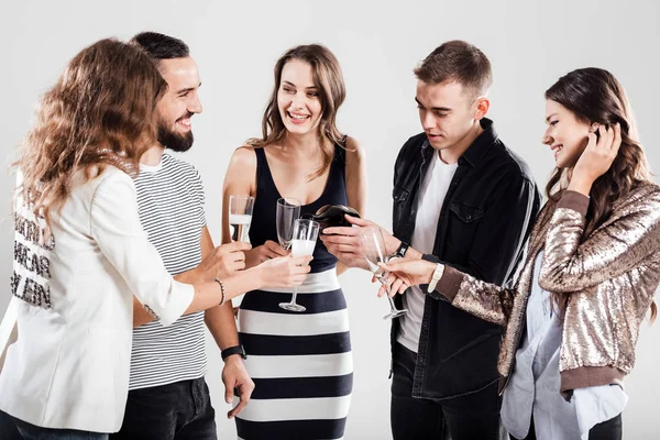 Girls and guys dressed in stylish casual clothes stand together and smile. Guy is pouring champagne in glasses. Party time