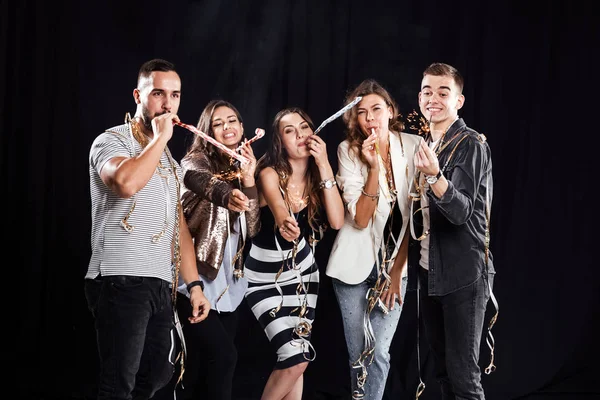 Hora da festa. Empresa de amigos na moda roupas casuais estão se divertindo com fitas e tubos e faíscas em um fundo preto no estúdio — Fotografia de Stock