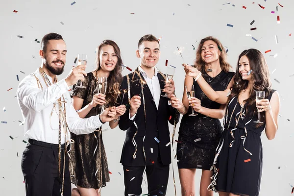 Company of  girls and guys dressed in stylish elegant clothes have fun together holding glasses of champagne and sparkles in hands on the white background confiture around. Party time .