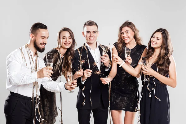 Compañía de chicas y chicos vestidos con ropa elegante y elegante se divierten juntos sosteniendo copas de champán y destellos en las manos en el confiture fondo blanco alrededor. Tiempo de fiesta — Foto de Stock