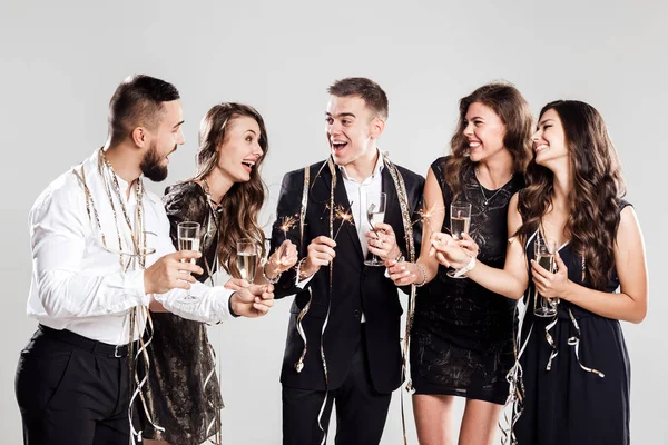 Compañía de chicas y chicos vestidos con ropa elegante y elegante se divierten juntos sosteniendo copas de champán y destellos en las manos en el confiture fondo blanco alrededor. Tiempo de fiesta — Foto de Stock