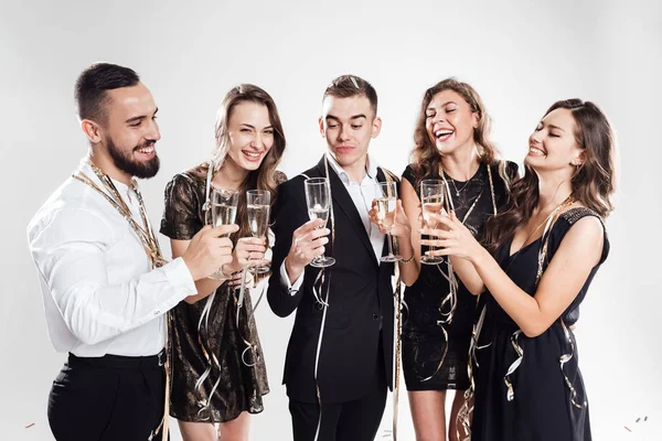 Tres chicas y dos tíos vestidos con ropa elegante y elegante se unen y golpean las copas con champán sobre el fondo blanco. Tiempo de fiesta — Foto de Stock