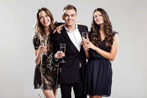 Hora de la fiesta. Dos hermosas chicas vestidas con elegantes vestidos elegantes y un hombre guapo en la sonrisa camisa blanca y sostener las copas de champán — Foto de Stock