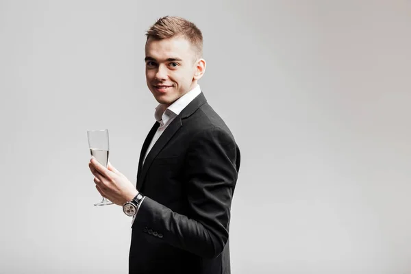 Homem bonito em um terno de negócios sorri e segura uma taça de champanhe em um fundo branco. Hora da festa — Fotografia de Stock