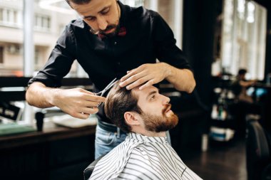 Kuaför kırmızı papyon ile siyah bir gömlek giymiş bıyıklı bir berber dükkanı genç adam için şık bir saç modeli yapar