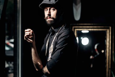 Bıyık ve sakal çözülmüş papyon ve düz kapak ile siyah bir gömlek giymiş şık Kuaför bir berber dükkanı karanlık odada duruyor