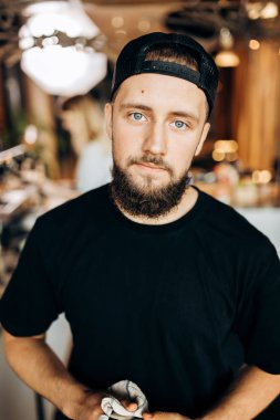 Yakışıklı bir genç şık adam sakallı, gündelik kıyafeti giymiş standları ve kameranın rahat bir kafede bakar.