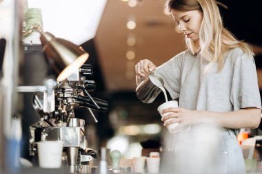 İyi görünümlü ince sarışın gündelik kıyafeti giymiş uzun saçlı modern bir kafede kahve pişiriyor. Kahve yapma süreci gösterilir.