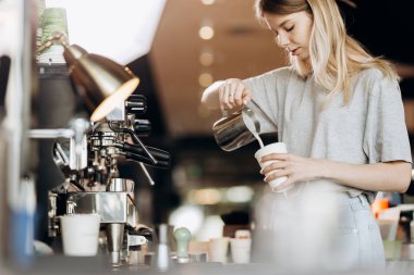 İyi görünümlü ince sarışın gündelik kıyafeti giymiş uzun saçlı modern bir kafede kahve pişiriyor. Kahve yapma süreci gösterilir.