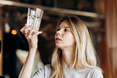 Gündelik kıyafeti giymiş genç bir ince sarışın dikkatle temiz bardak sıcak bir kahve dükkanında bakıyor.