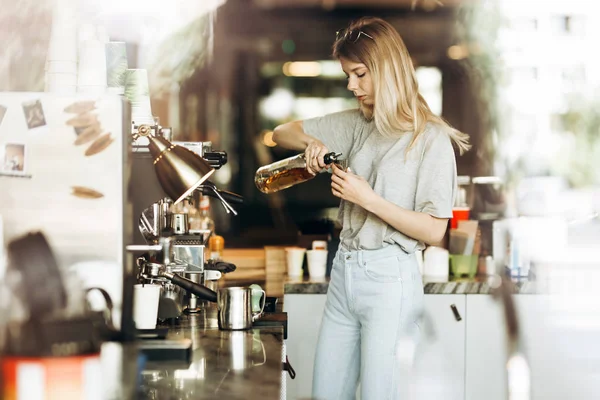 Młoda Blondynka dość cienkie, z długimi włosami, ubrany w strój casual, jest gotowanie kawy w nowoczesną kawiarnię. Przedstawiono proces parzenia kawy. — Zdjęcie stockowe