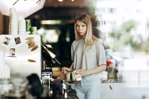 Mladá krásná tenké Blondýna s dlouhými vlasy, oblečen v neformální oblek, je vaření kávy v moderní kavárně. Je zobrazen proces vaření kávy. — Stock fotografie