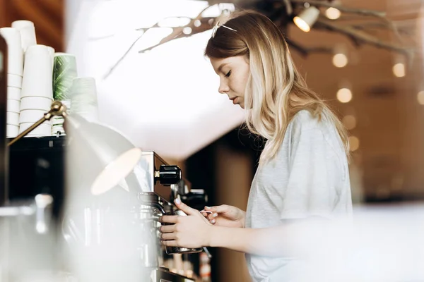 Dobře vypadající štíhlá blondýnka s dlouhými vlasy, oblečen v neformální oblek, je vaření kávy v moderní kavárně. Je zobrazen proces vaření kávy. — Stock fotografie