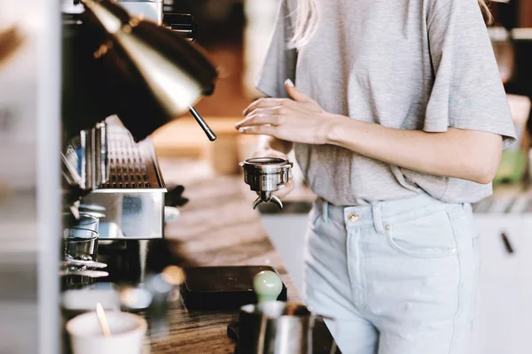 Гарна струнка блондинка з довгим волоссям, одягнена в повсякденне вбрання, готує каву в сучасному кафе. Показано процес приготування кави . — стокове фото