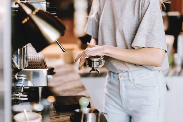 Eine gut aussehende, schlanke Blondine mit langen Haaren, in lässigem Outfit, kocht Kaffee in einem modernen Café. Prozess der Kaffeezubereitung wird gezeigt. — Stockfoto