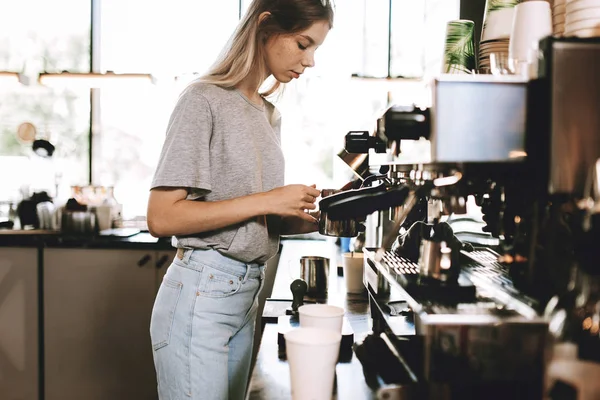 Молода досить тонка блондинка, одягнена в повсякденне вбрання, готує каву в популярній кав'ярні . — стокове фото