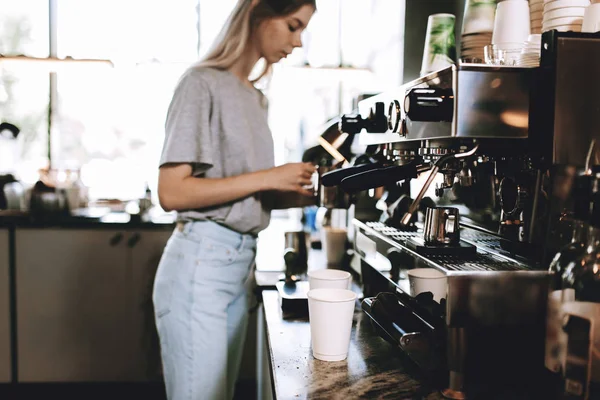 Молода досить тонка блондинка, одягнена в повсякденне вбрання, готує каву в популярній кав'ярні . — стокове фото