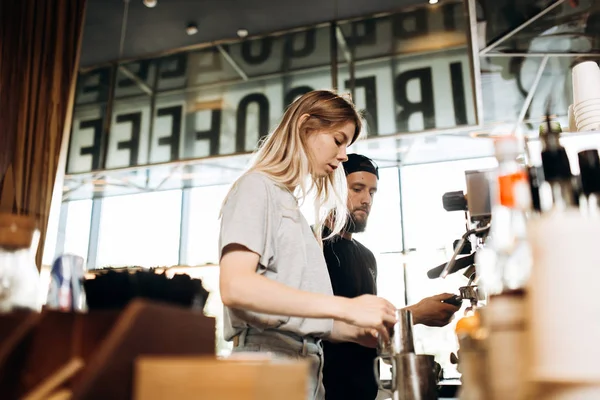 Два молодих бариста, блондинка і стильний чоловік з бородою, показали приготування кави разом у кавовій машині в затишній кав'ярні . — стокове фото