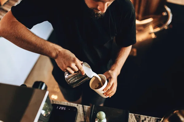 A stylish young man with beard,wearing casual outfit,is shown in the process of cooking coffee in a cozy coffee shop. — Stock Photo, Image