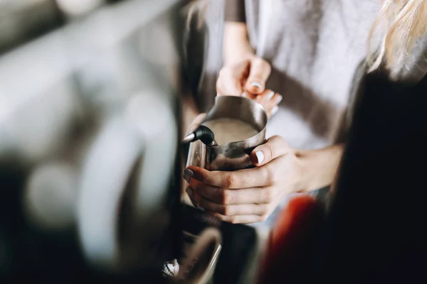 Uma menina loira bonita magro jovem, vestida com roupa casual, está segurando uma espuma de leite em uma loja de café aconchegante . — Fotografia de Stock