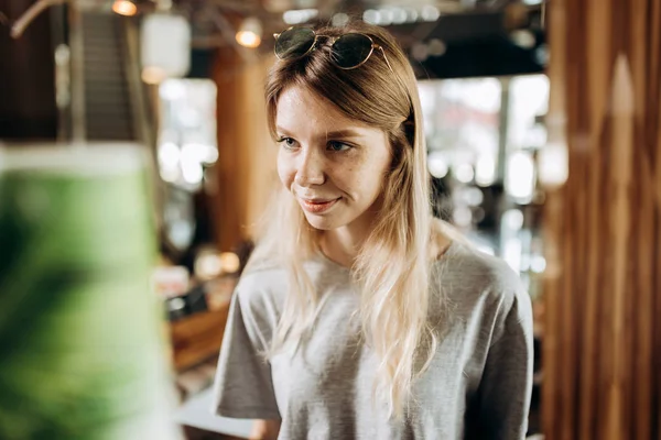 一个漂亮的年轻苗条的女孩, 穿着休闲的风格, 站在旁边的咖啡机和微笑在一个舒适的咖啡店. — 图库照片