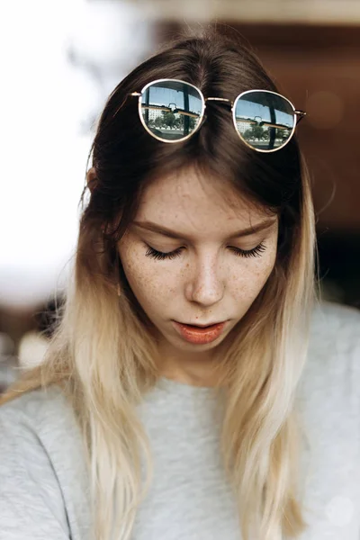 Uma linda loira magra com óculos, vestida com roupas casuais, está sentada e olhando para baixo em um aconchegante café . — Fotografia de Stock