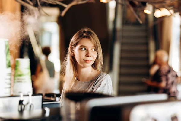 Usmívající se roztomilý mladý Blondýnka, ležérní oblečení na sobě, stojí u automatu na kávu a dívá na okna, — Stock fotografie