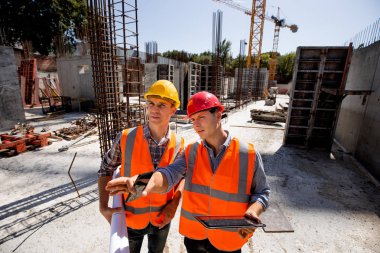 İnşaat mühendisi ve mimar turuncu iş yeleği giymiş ve açık şantiye İnşaat malzeme ile inşaat süreci zor yarasalar tartışmak