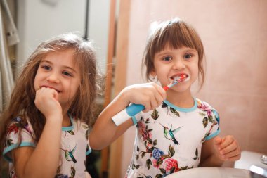 İki küçük güzel kız kardeş aynı gömlek fırça onların dişler banyoda giyinmiş