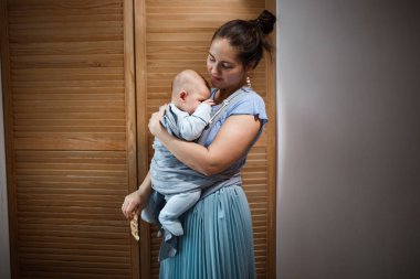 Genç Anne ışık mavi t-shirt giymiş ve etek küçük oğlu ahşap kapı yanındaki odada kollarındaki tutuyor