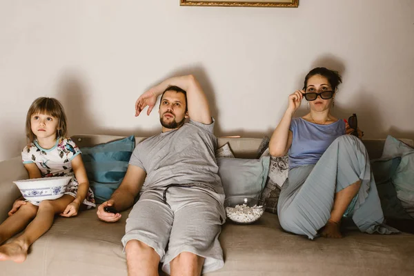 Πατέρα, μητέρα και κόρη, βλέποντας τηλεόραση και τρώγοντας ποπ κορν που κάθεται στον καναπέ — Φωτογραφία Αρχείου
