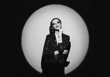 Siyah beyaz portre saç geri çekti ve bir parlayan elbise kapının g parlak spot duvarda yanında şık makyaj ile trendy kız