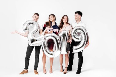 Neşeli iki kız ve şık giysilerle giyinmiş iki adam balon numaraları 2019 stüdyoda beyaz bir arka plan üzerinde şeklinde tutuyor