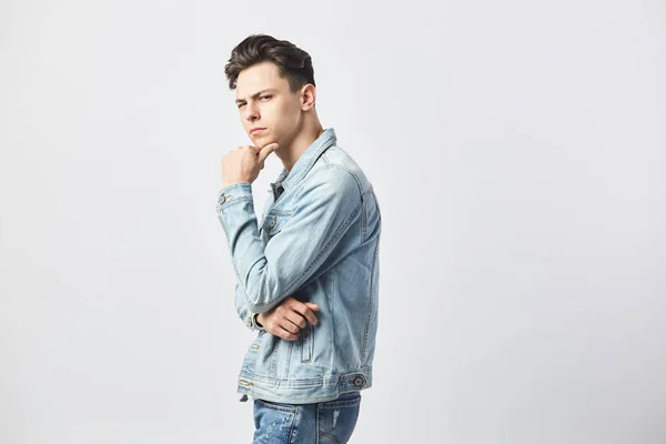 Homme aux cheveux bruns habillé d'un t-shirt blanc et d'une veste en denim se tient sur le fond blanc dans le studio — Photo