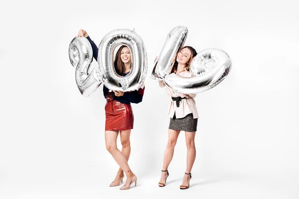 Dos hermosas chicas vestidas con una elegante ropa inteligente están sosteniendo globos en forma de números 2019 sobre un fondo blanco en el estudio — Foto de Stock