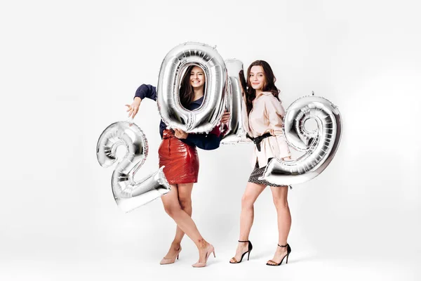 Duas meninas bonitas vestidas com uma elegante roupa inteligente estão segurando balões na forma de números 2019 em um fundo branco no estúdio — Fotografia de Stock