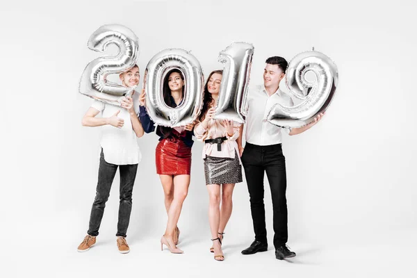 Feliz amigos dos chicas y dos chicos vestidos con ropa elegante están sosteniendo globos en forma de números 2019 sobre un fondo blanco en el estudio — Foto de Stock